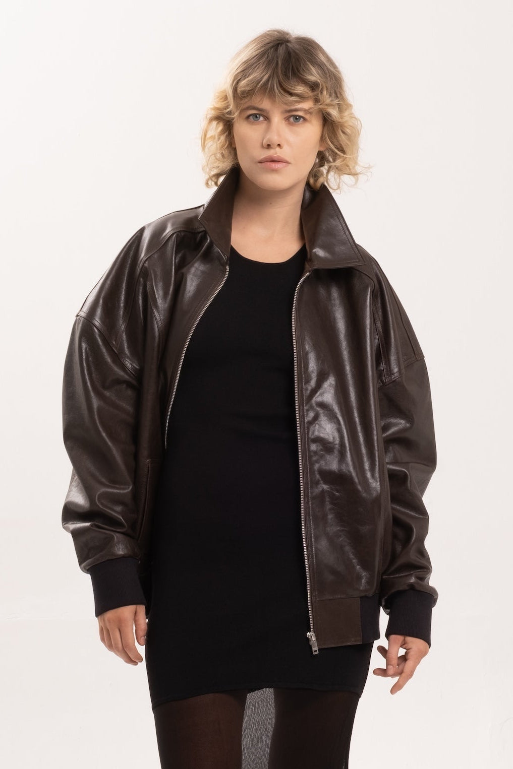 Person wearing a brown leather jacket and black dress on a white background